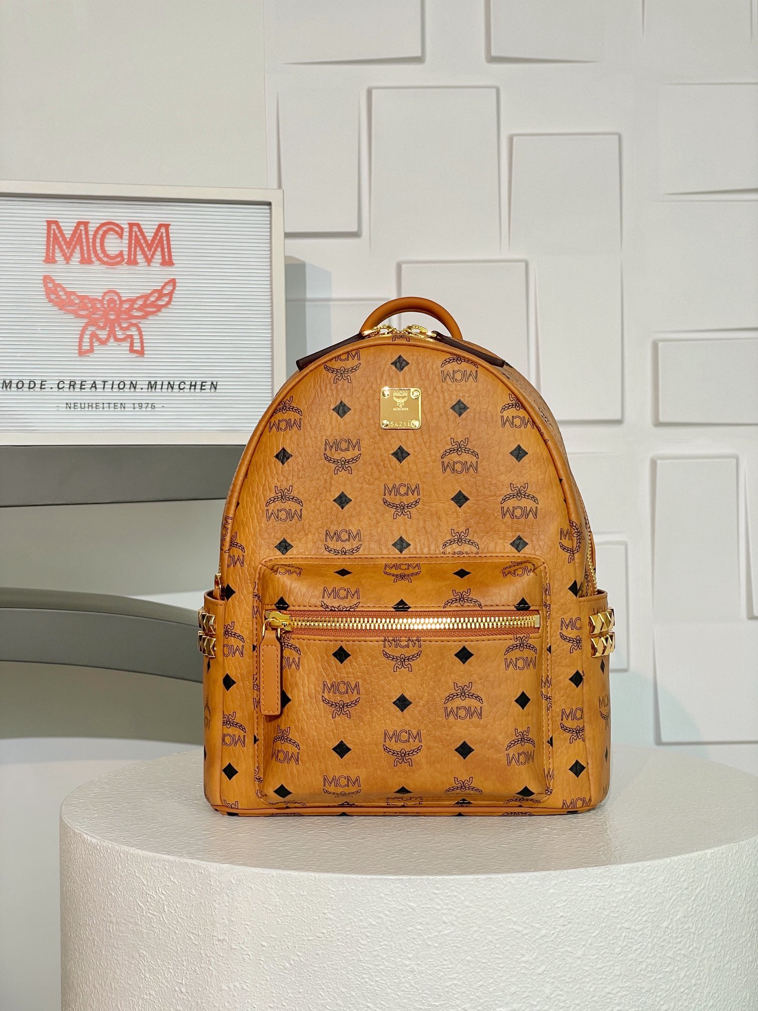 MCM Strak Visetos Cognac Small Studded Backpack: MCM Strak Visetos Cognac Small Studded Backpack. This luxurious backpack features a well-structured design, crafted from classic Visetos material and trimmed with luxurious Nappa leather. Its spacious