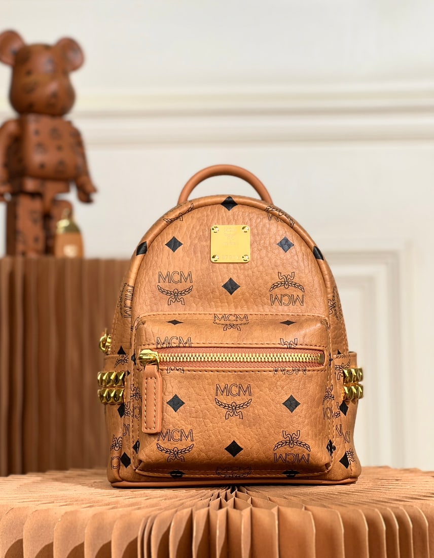 MCM Strak Visetos Mini Studded Backpack: The MCM Strak Visetos Mini Studded Backpack, in classic cognac, is officially called the mini size. This classic Stark backpack, crafted from the Visetos pattern and Nappa leather, is a pioneering pie