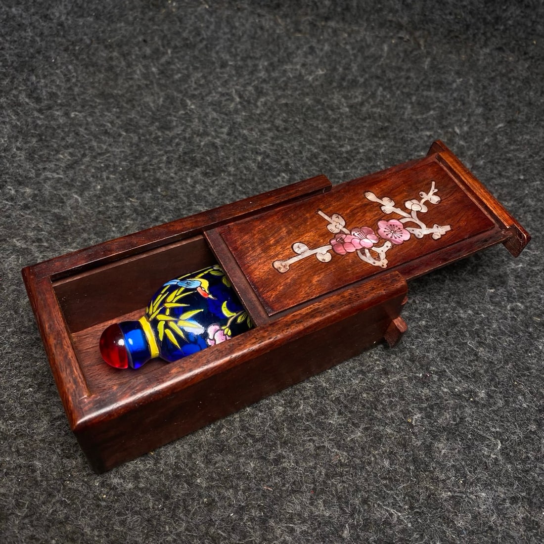 A rosewood box inlaid with mother-of-pearl contains an antique glass snuff bottle.: A rosewood box inlaid with mother-of-pearl contains an antique glass snuff bottle. The snuff bottle's dimensions are: 3.8/2.5/8cm (L/W/H). The box's dimensions are: 12/6/4.5cm (L/W/H). Provenance:From