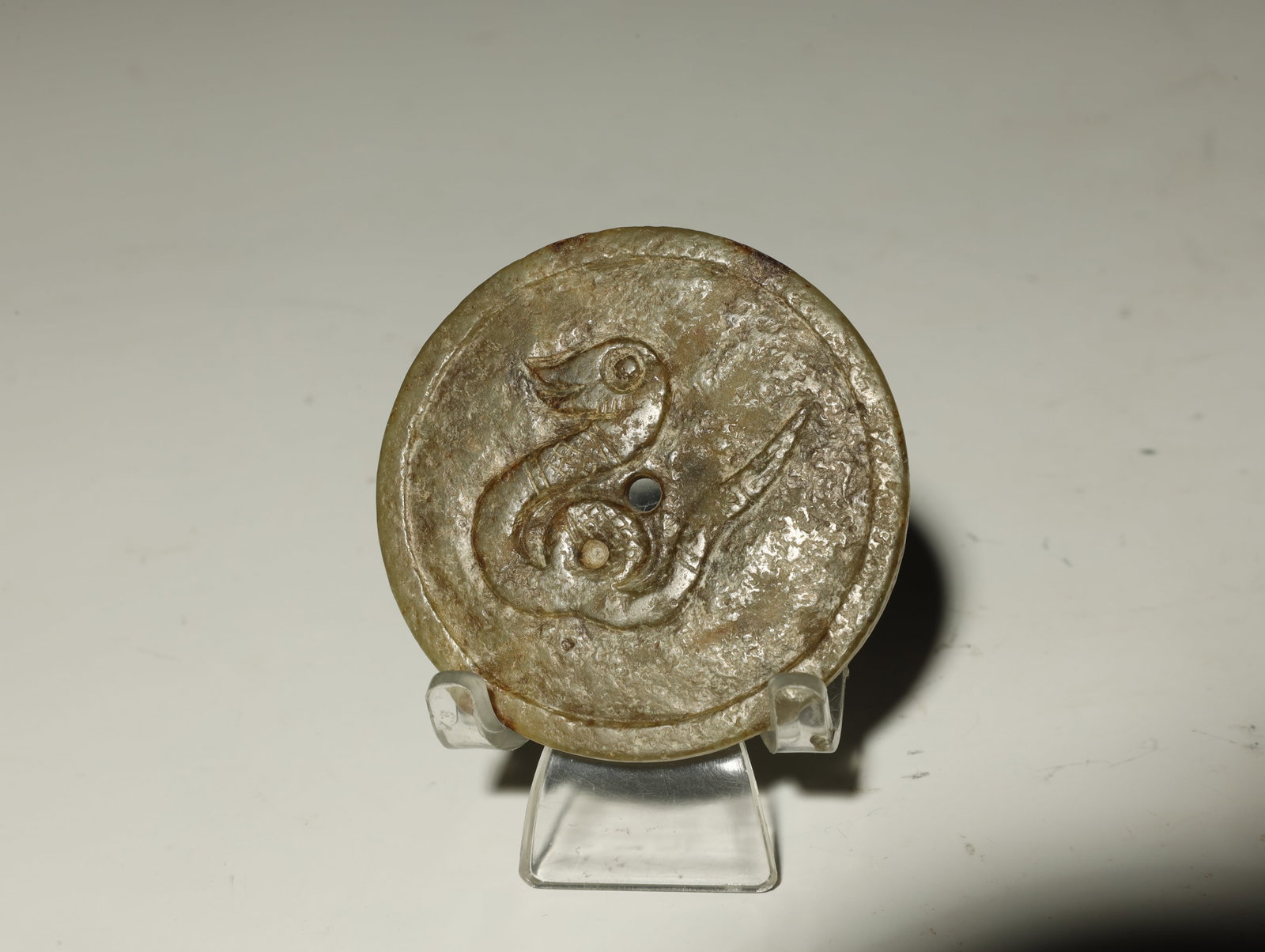 AN IMPRESSIVE LATE SHANG TO WESTERN ZHOU DYNASTY ROUND JADE PLAQUE: AN IMPRESSIVE LATE SHANG TO WESTERN ZHOU DYNASTY ROUND JADE PLAQUE WITH COILED SERPENT DESIGN. Chinese, circa 1200–800 BCEDiameter 6 cm. Description: Carved in shallow relief from gray?green nephrit