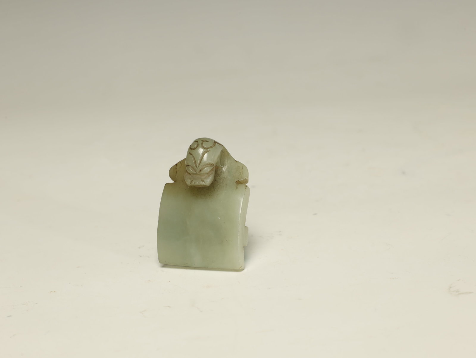 Han Dynasty PALE CELADON AND RUSSET JADE: A HANDSOME PALE CELADON AND RUSSET JADE 'CHI-DRAGON' SWORD SLIDE (JIAN BI)Han Dynasty (206 BC – AD 220)Length 5 cm × Width 3.5 cmDescription: A small archaistic jade sword fitting of arched rectang