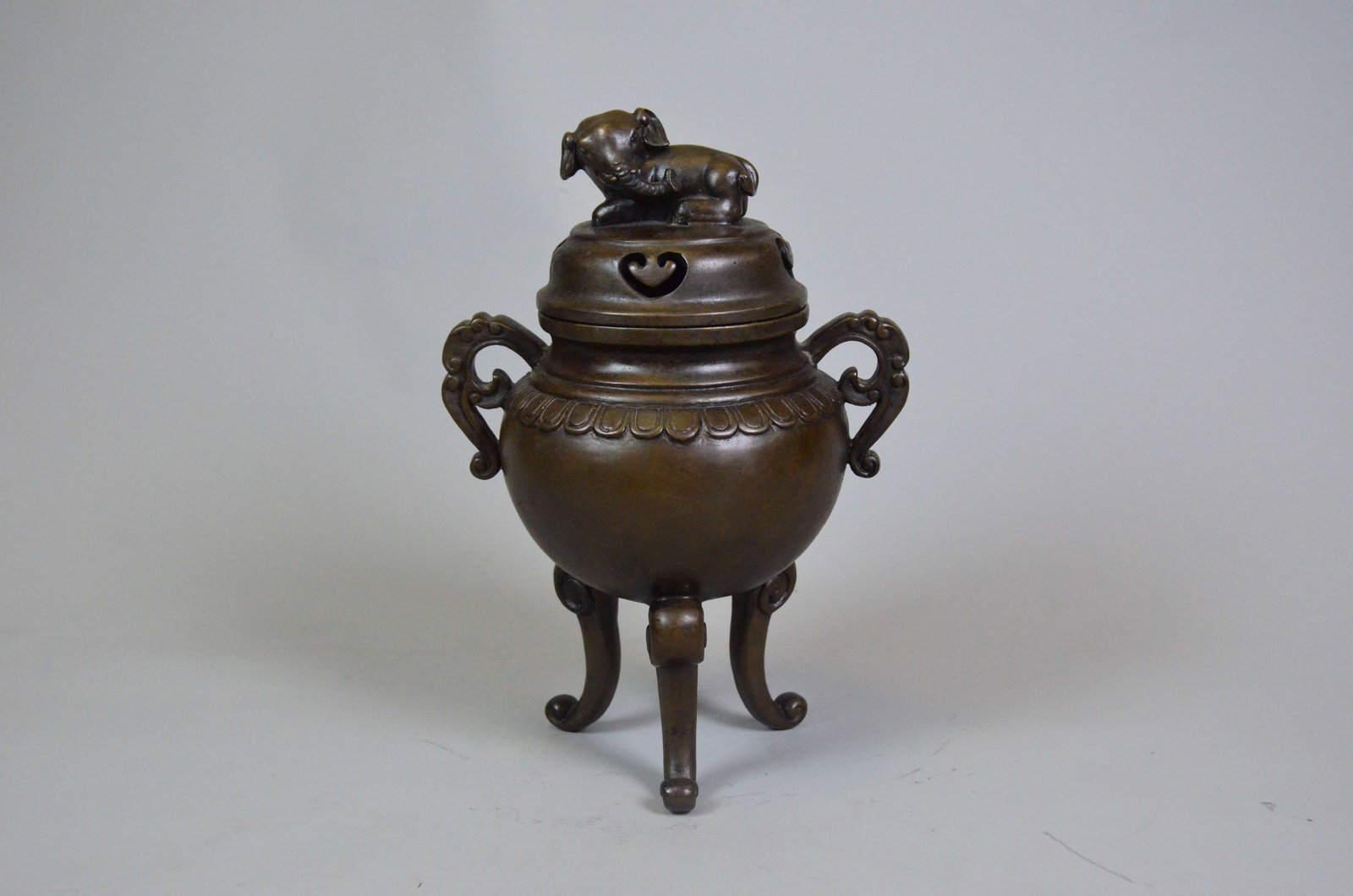 Qing Dynasty Bronze Scroll-Handle Tripod Censer: Qing Dynasty Bronze Scroll-Handle Tripod Censer with Elephant FinialQing DynastyHeight: 27cm Mouth Diameter: 10cmDescription: A tripod censer with a compressed globular body flanked by a pair of plain