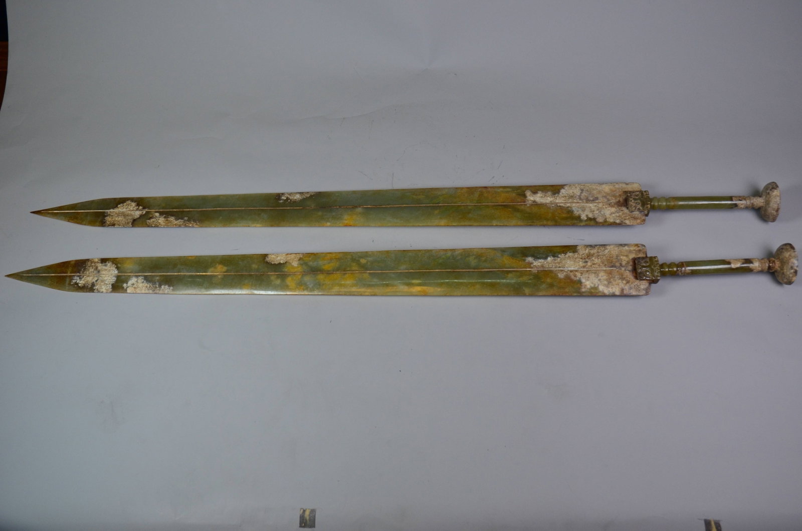 Warring States Period Ceremonial Hetian Jade: Warring States Period Hetian Jade Swords, PairWarring States PeriodLength: 110cm Width: 8cm Depth: 0.3cmDescription: A pair of flat, tapering ceremonial swords carved entirely from a single piece of s