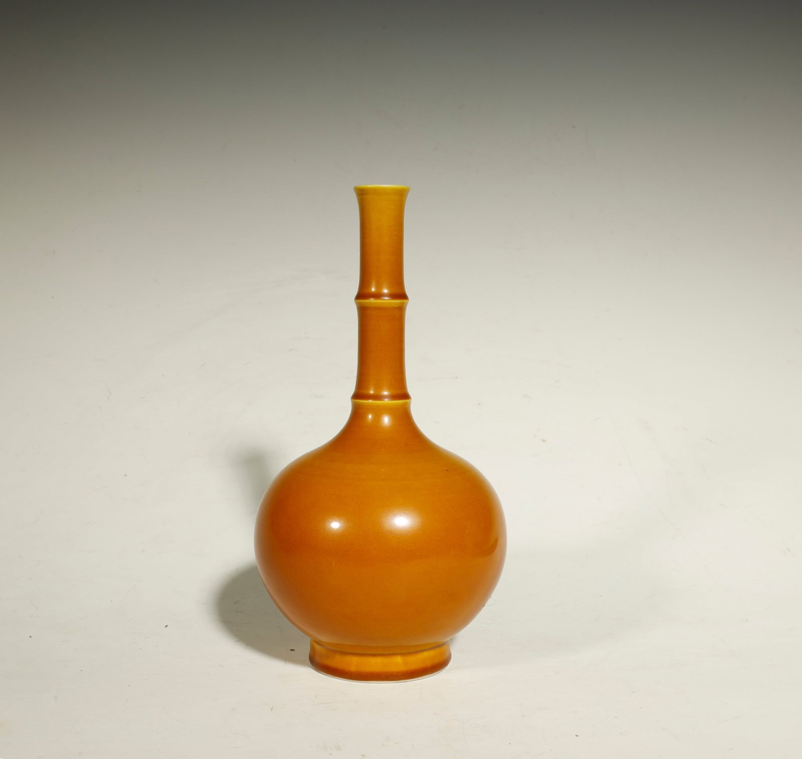 Qing DynastyTurmeric Amber-Glazed Bamboo-stemmed: A Turmeric Amber-Glazed Bamboo-stemmed Bottle VaseChina, Qing DynastyHeight: 7.3 in. (18.5 cm)Description: A porcelain bottle vase of compressed globular form with a tall waisted neck divided by a rai