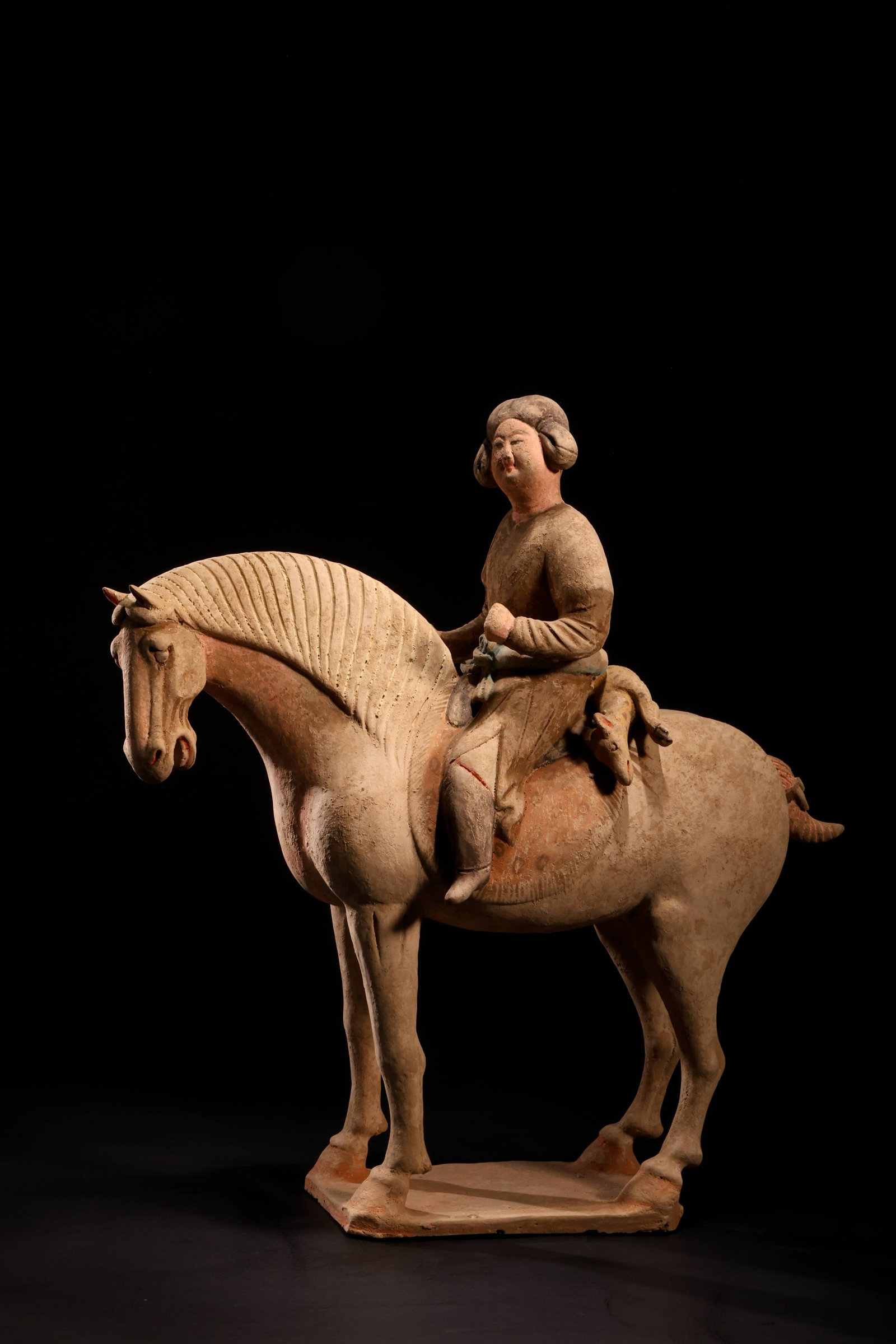 Tang Dynasty Court Lady on Horseback Figurine: Tang Dynasty Court Lady on Horseback FigurineTang Dynasty (618-907 AD)Height: 36cm Length: 34cmDescription: A pottery figure of a plump-cheeked court lady seated astride a standing horse, her hair dre