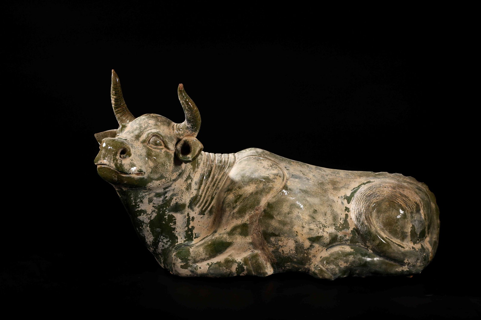 Han Dynasty Green-Glazed Pottery Ox: Han Dynasty Green-Glazed Pottery OxHan Dynasty (206 BC-220 AD)Height: 29cm Length: 46cmDescription: A pottery figure of a recumbent ox, its legs folded beneath its body, the head raised and turned sli