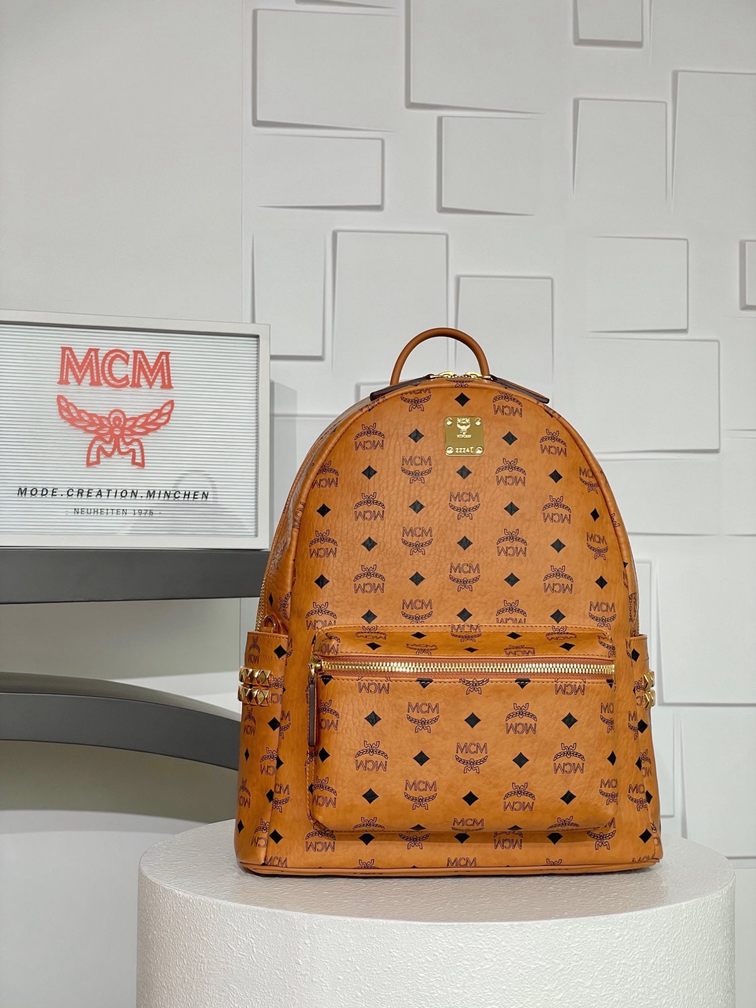 MCM Strak Visetos Cognac Medium Studded Backpack: MCM Strak Visetos Cognac Medium Studded Backpack. This luxurious backpack features a well-structured design, crafted from classic Visetos material and trimmed with luxurious Nappa leather. Its spaciou