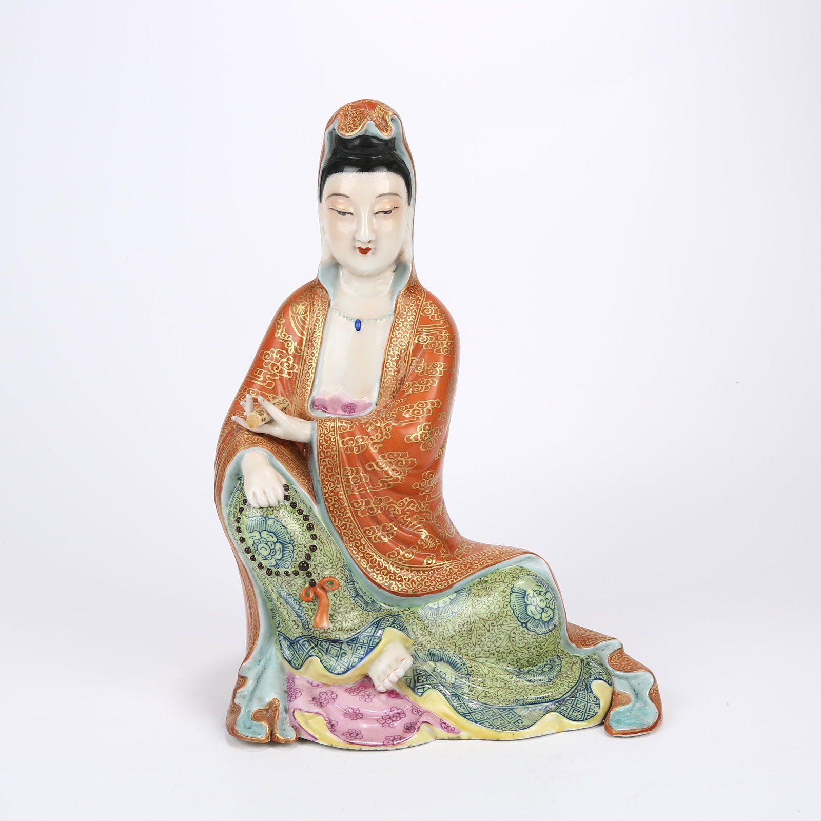 A FAMILLE ROSE SEATED GUANYIN HOLDING A SCRIPTURE: Famille rose seated Guanyin holding a scripture