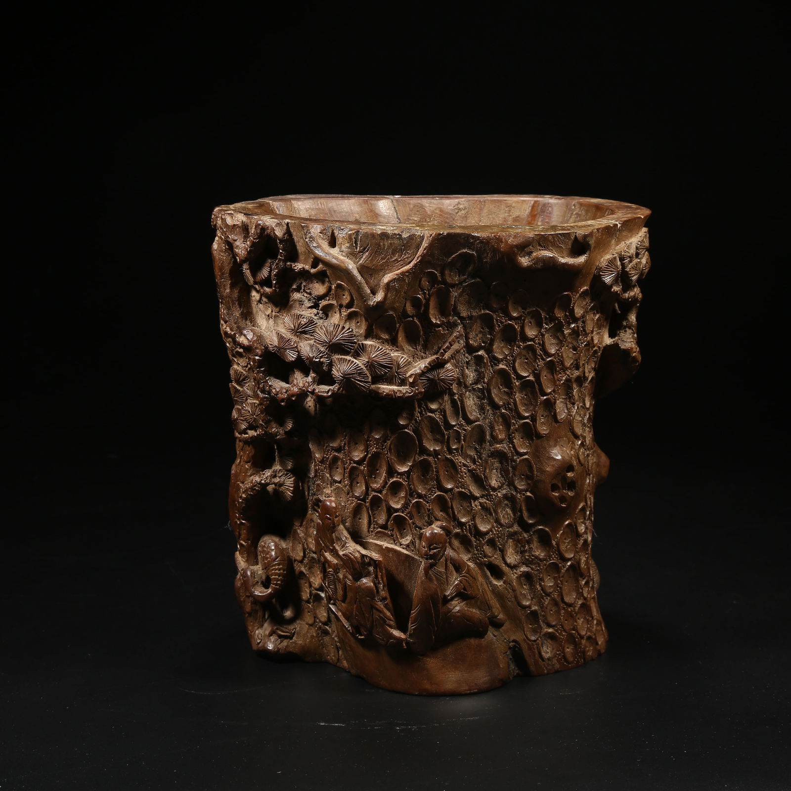 A HUANGHUALI WOOD BRUSH POT SHAPED LIKE A TREE STUMP WITH A HIGH OFFICIAL UNDER PINE TREES: Huanghuali wood brush pot shaped like a tree stump with a high official under pine trees
