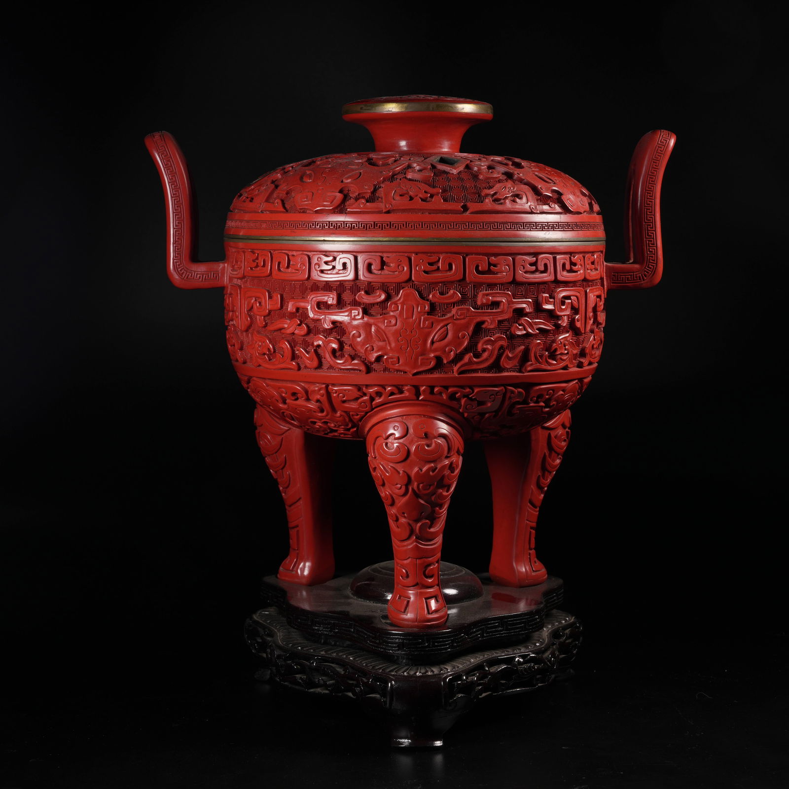A CARVED RED-LACQUER THREE-FOOTED CENSER WITH BEAST-FACE MOTIF AND IMPERIAL CROWN HANDLES: Carved red-lacquer three-footed censer with beast-face motif and imperial crown handles