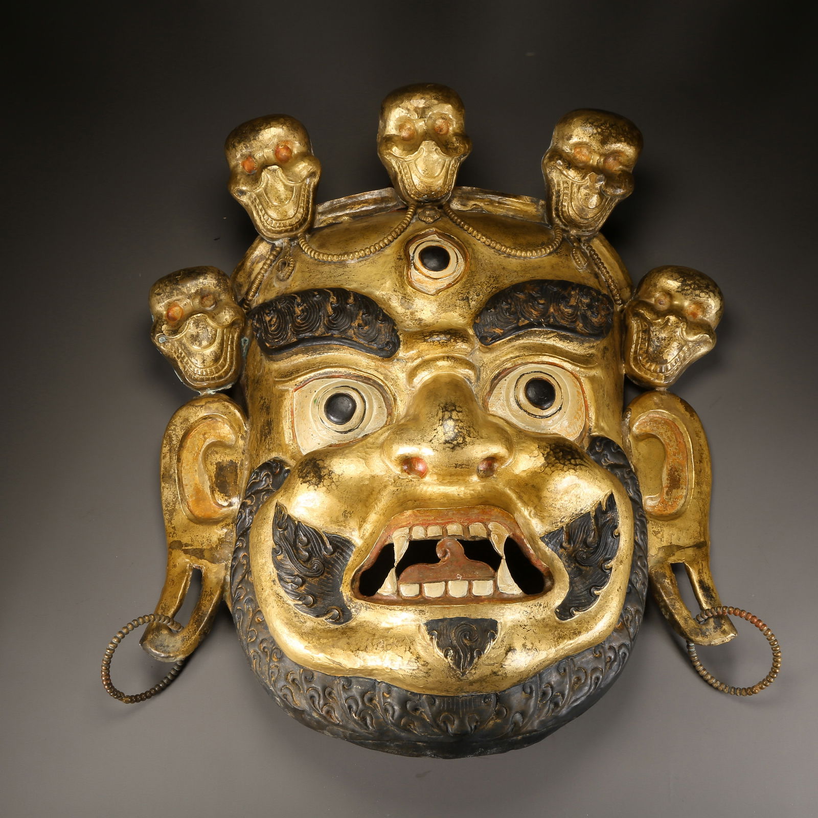 A GILDED BRONZE HAMMERED DHARMAPALA HEAD PENDANT: Gilded bronze hammered Dharmapala head pendant