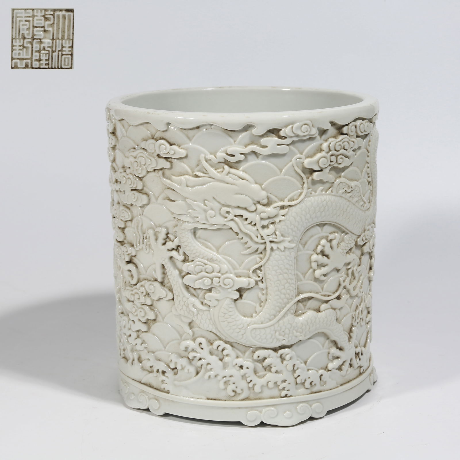 A WHITE-GLAZED CARVED PORCELAIN BRUSH POT WITH CLOUD AND DRAGON PATTERN: White-glazed carved porcelain brush pot with cloud and dragon pattern