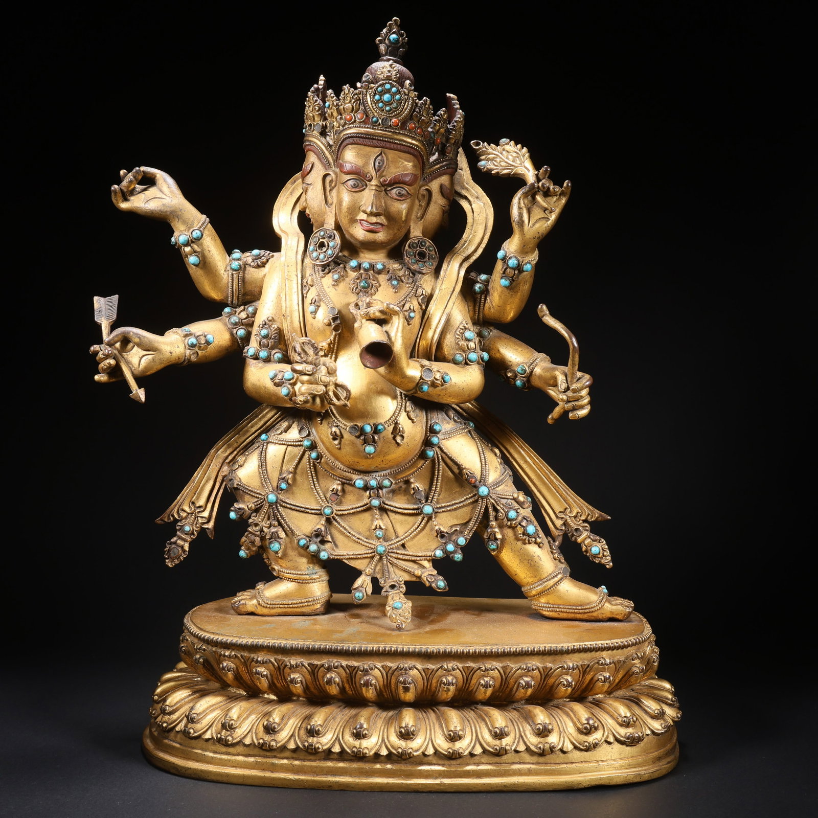 A GILT-BRONZE, GEM-INLAID DHARMA PROTECTOR STATUE WITH THREE HEADS AND SIX ARMS: Gilt-Bronze, Gem-Inlaid Dharma Protector Statue with Three Heads and Six Arms