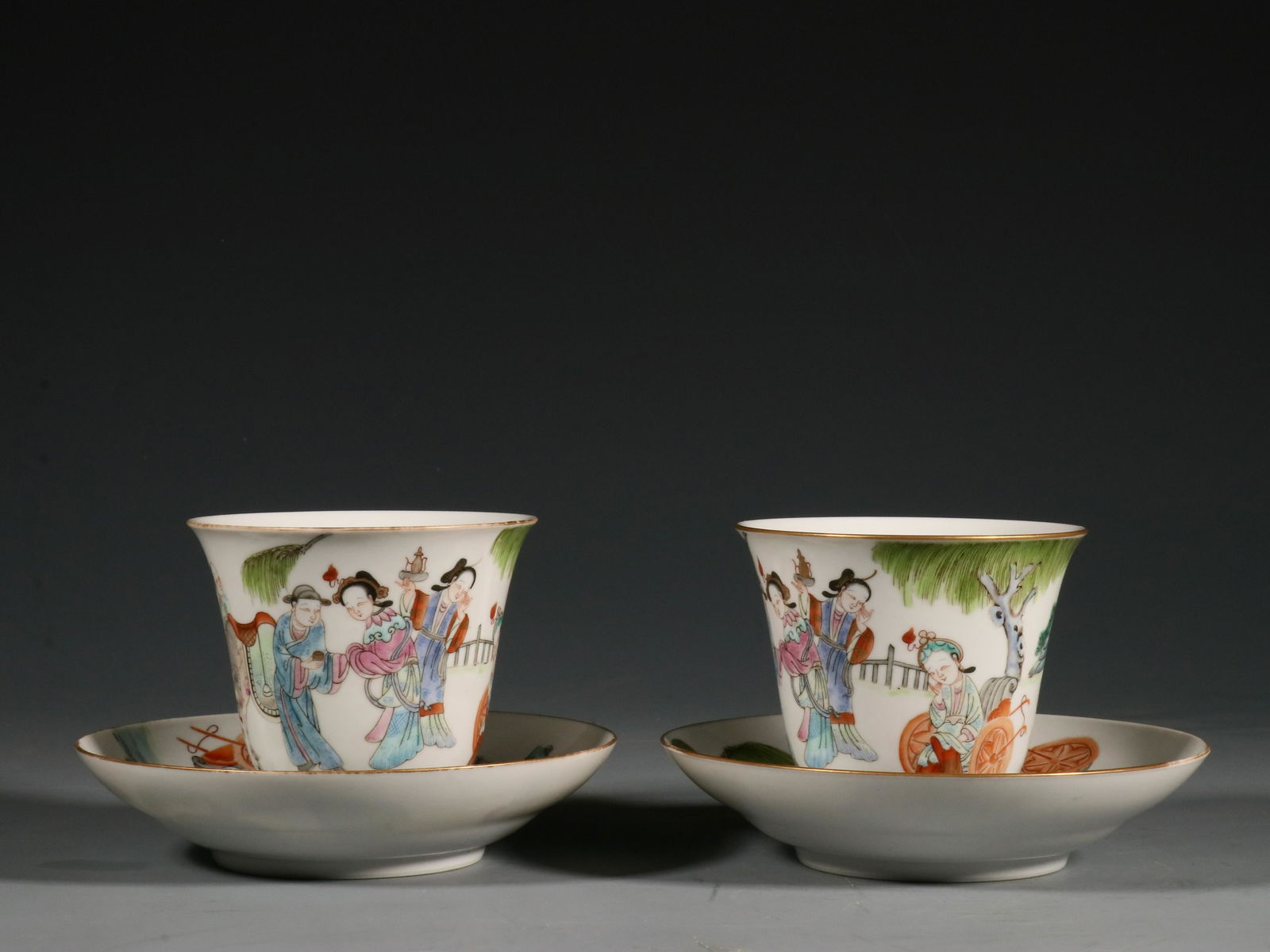 A PAIR OF PASTEL GOLD CHARACTER STORY CUPS: The cup has a height of 7.3cm and a diameter of 8.3cm. Cup holder size: 3cm high, 12.8cm diameter.