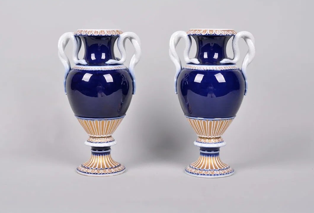 19th Century Meissen Snake Handle Vases, German: A striking pair of Meissen porcelain urns, each of amphora form with a rich cobalt blue body, fluted lower section highlighted in gilt and ochre, and raised on a pedestal base. The urns are surmounted