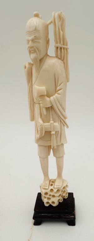 Chinese Carved Figure of an ElderRepublic Pd: A finely carved figure of a Chinese elder or sage, standing barefoot on a pierced rocky base and mounted on a fitted hardwood stand. The figure is depicted with a long beard and topknot, holding an ax