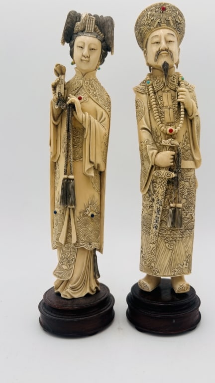 Pair of Chinese Carved Figures of an Emperor Elephant tusk: A fine pair of intricately carved figures, representing an Emperor and Empress, each standing on a fitted hardwood base. Both figures are richly adorned in ornately decorated robes with incised cloud 