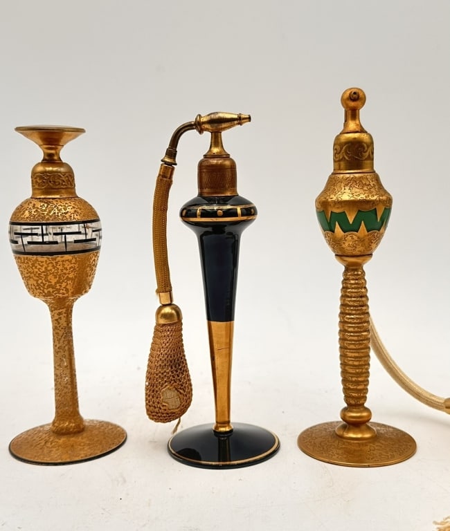 Set of Art Deco Gilded Glass Perfume Atomizers A group of three Art Deco gilt and enamel glass: A group of three Art Deco gilt and enamel glass perfume bottles/atomizers, each of elegant elongated form on a circular base:One with geometric black-and-white Greek key enamel band,One with black lac