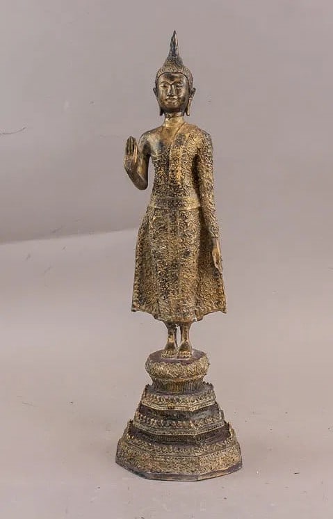 Thai bronze carved Buddha sculpture, standing on a tiered pedestal base with right hand raised in: Thai bronze carved Buddha sculpture, standing on a tiered pedestal base with right hand raised in Abhaya mudra and left hand resting at side. Figure features elongated earlobes, ushnisha, and patterne