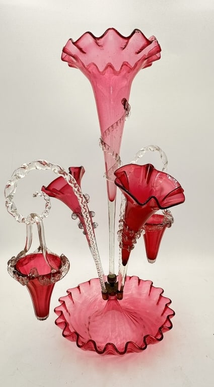 A fine hand-blown cranberry glass epergne comprising a central fluted trumpet vase surrounded by: A fine hand-blown cranberry glass epergne comprising a central fluted trumpet vase surrounded by three smaller matching trumpets and a hanging basket, all rising from a ruffled circular bowl base. The