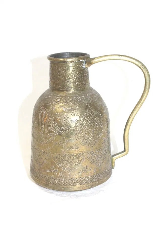 An Ottoman brass ewer, 18th/19th century. Of tapering cylindrical form with a tall neck and: An Ottoman brass ewer, 18th/19th century. Of tapering cylindrical form with a tall neck and angular handle, finely engraved with panels of interlaced arabesques, geometric latticework, and calligraphi