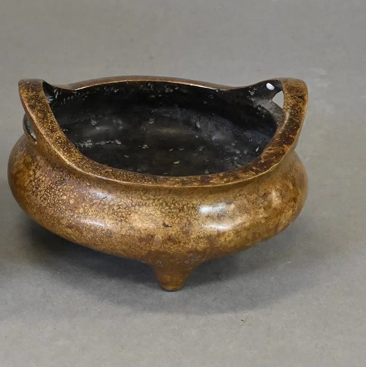 Chinese Bronze Tripod Censer with Xuande Mark Cast bronze censer of rounded form with two upright: Chinese Bronze Tripod Censer with Xuande Mark Cast bronze censer of rounded form with two upright loop handles and raised on three short feet. The body displays a mottled golden-brown patina from age