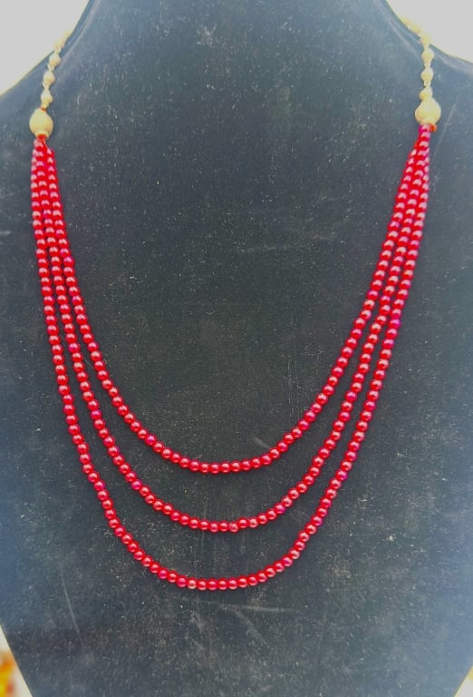 A vibrant necklace composed of multiple strands of polished ruby beads in a rich translucent red: A vibrant necklace composed of multiple strands of polished ruby beads in a rich translucent red hue, strung in uniform rows that shimmer with light. The strands are accented with silver beads and sph
