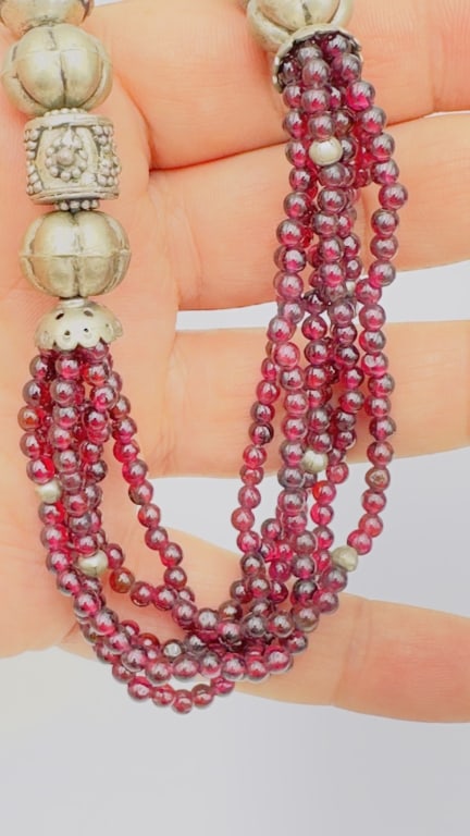 A striking necklace composed of multiple strands of polished deep-red garnet beads, interspaced: A striking necklace composed of multiple strands of polished deep-red garnet beads, interspaced with silver bead accents and finished with large ornate silver terminals. The garnets display a rich win