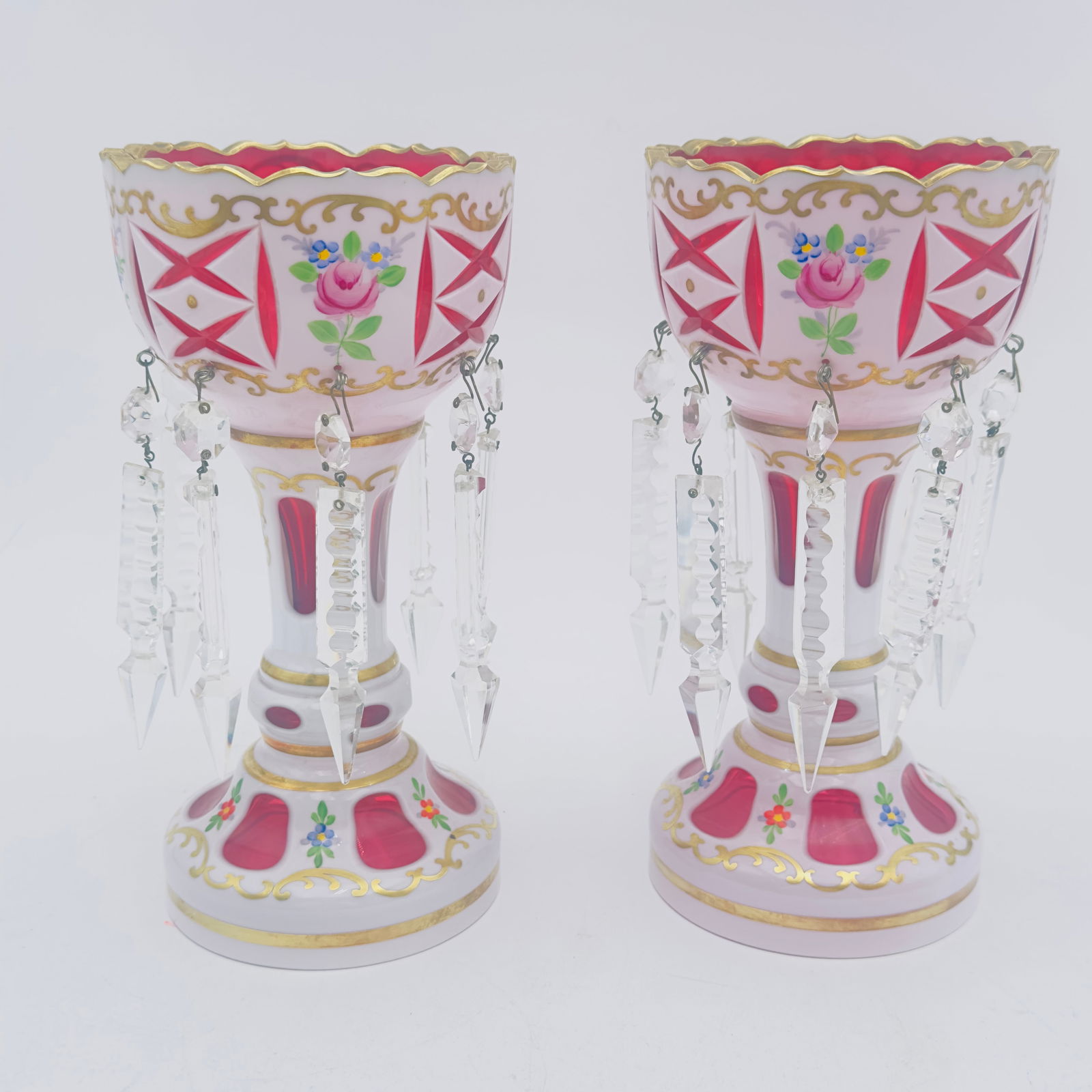 Pair of Bohemian Cranberry/Amber Glass Mantel Lustres, circa early 20th century: 19th century, gothic cut rim. A pair of Czech art glass mantle lustres with white overlay cut back to cranberry with staggered double hung crystal prisms and hand painted floral garland accents