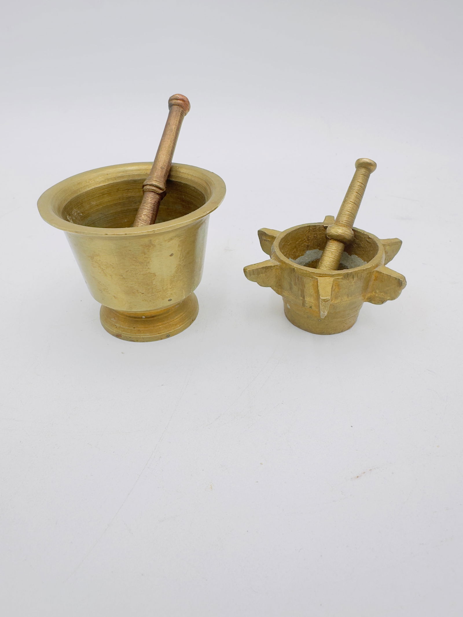 Pair of Vintage Brass Mortar & Pestles: A pair of vintage brass mortar and pestles in two sizes, including a traditional flared form and a decorative example with side projections. Suitable for culinary or decorative use.
