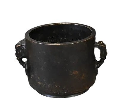 Cast bronze censer of cylindrical form with a flared rim and a pair of sculpted lion mask handles: Cast bronze censer of cylindrical form with a flared rim and a pair of sculpted lion mask handles at the sides. The vessel retains a dark brown patina with areas of wear consistent with age and use.