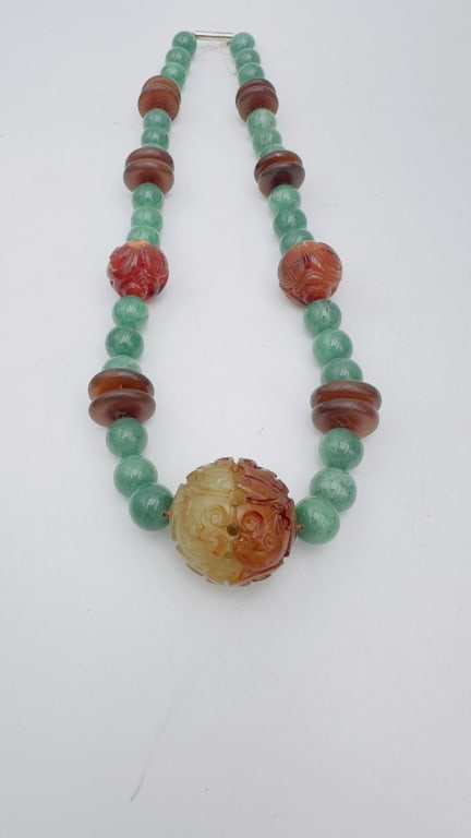 A striking necklace featuring a large central carved jade bead of mottled celadon and russet (1 of 7)