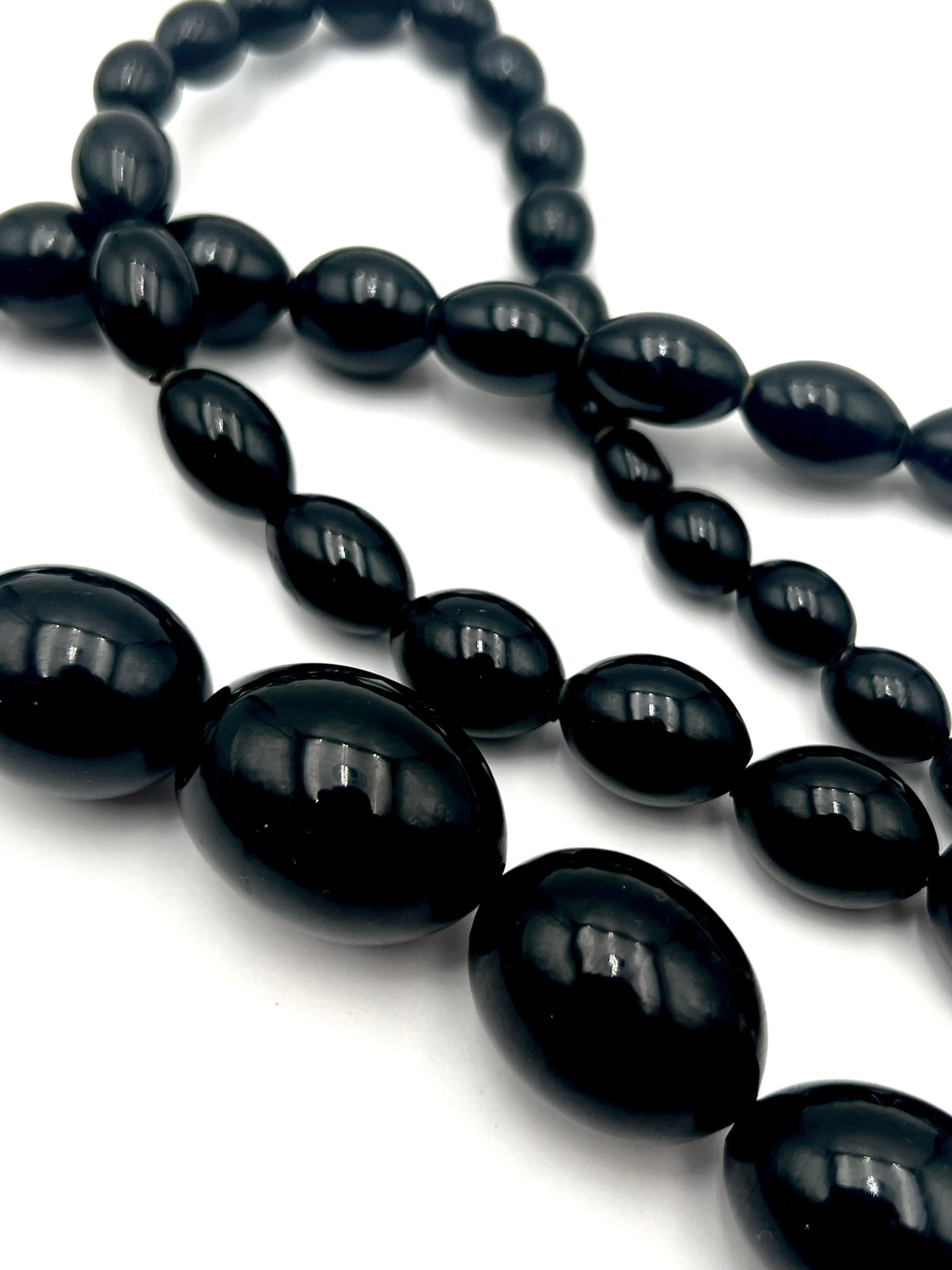 Vintage Black Bakelite Graduated Bead Necklace: A vintage necklace composed of tested black Bakelite beads in a graduated oval form. The beads display a deep rich black tone with a smooth polished glossy surface, hand-strung in a classic graduated 