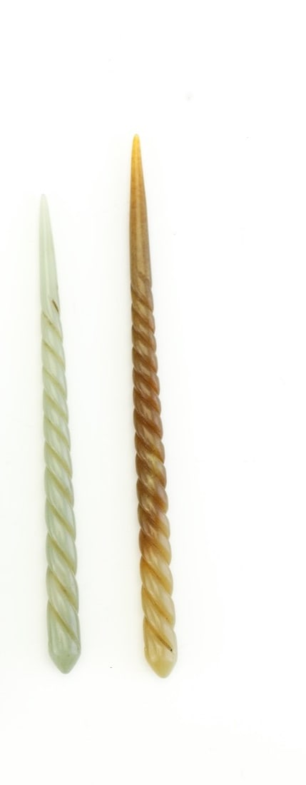 Two carved conical hair pin ornaments with spiraln A pair of carved hair pins in the traditional: A pair of carved hair pins in the traditional Chinese style, each featuring a twisted form with tapered ends. One example is rendered in a pale green stone, while the other displays warm amber-brown t