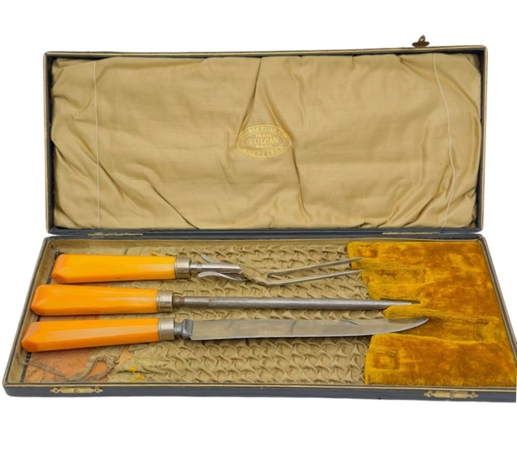 Vintage Sheffield Carving Set with Bakelite Handly A vintage three-piece carving set comprising a: A vintage three-piece carving set comprising a carving knife, carving fork, and sharpening steel, each fitted with faceted amber-colored Bakelite handles. The blades are of Sheffield manufacture, hous