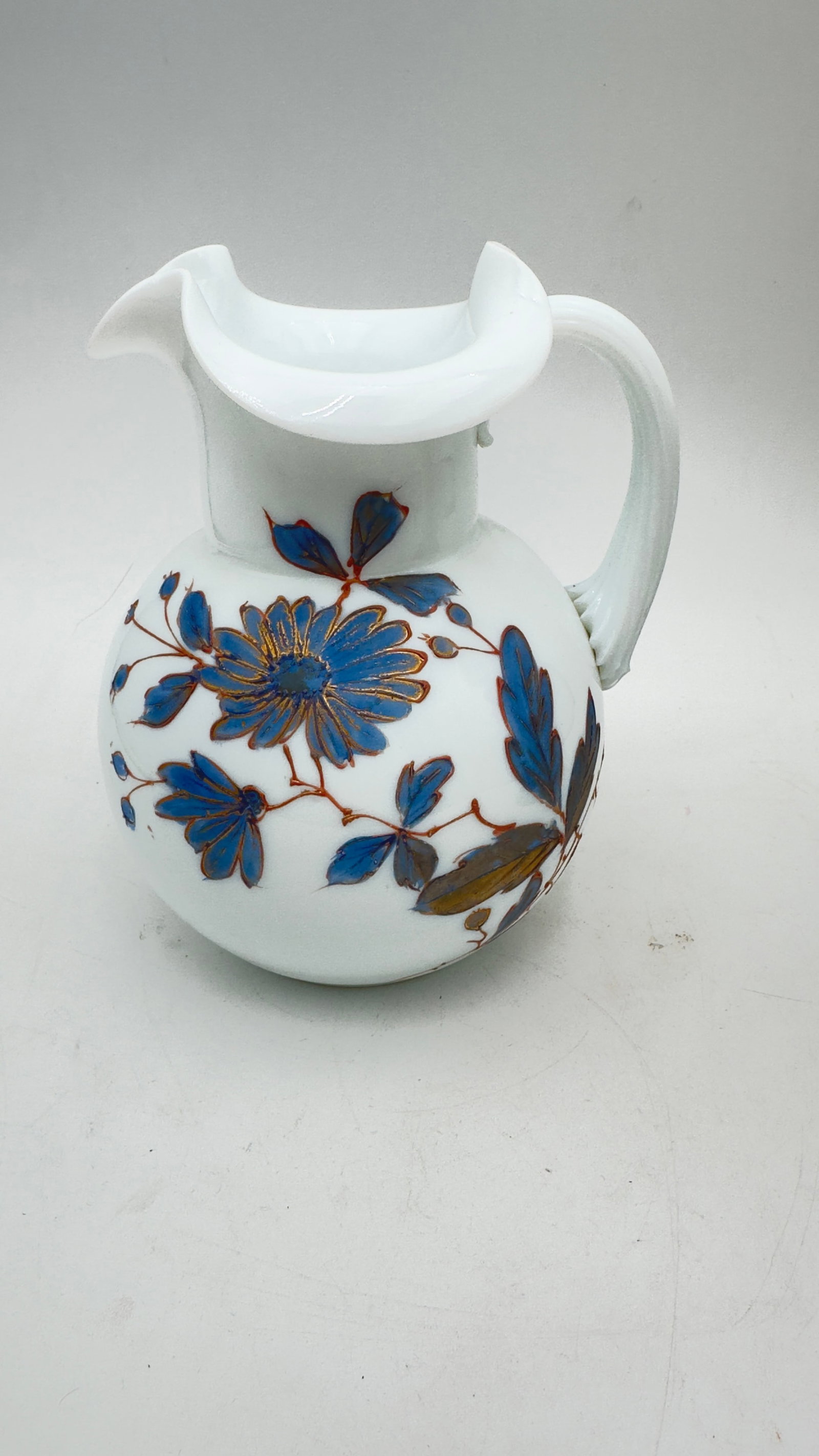 Bohemian Opaline Enameled Glass Pitcher, 20th Century: A charming Bohemian opaline glass pitcher, featuring a soft milky white body with a rounded form and applied handle. The surface is beautifully hand-decorated with polychrome floral enamel motifs in b