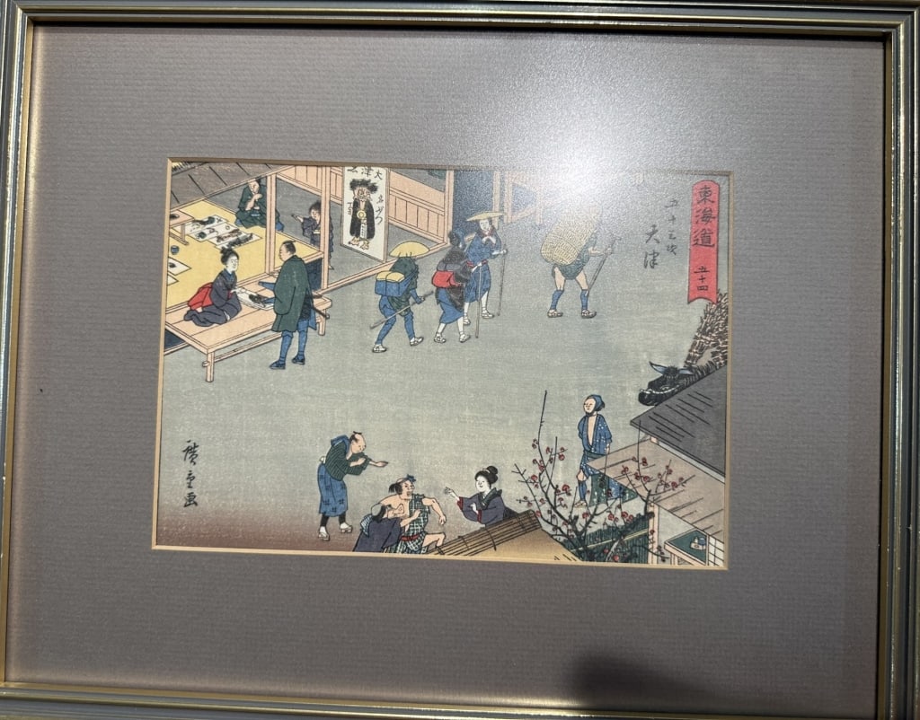 Antique Japanese Woodblock Print Scene with Travelers and Figures: A traditional Japanese woodblock print featuring a busy narrative street and shop scene with multiple figures, travelers, and architecture.Design & Motifs: Showcases a detailed outdoor composition wit