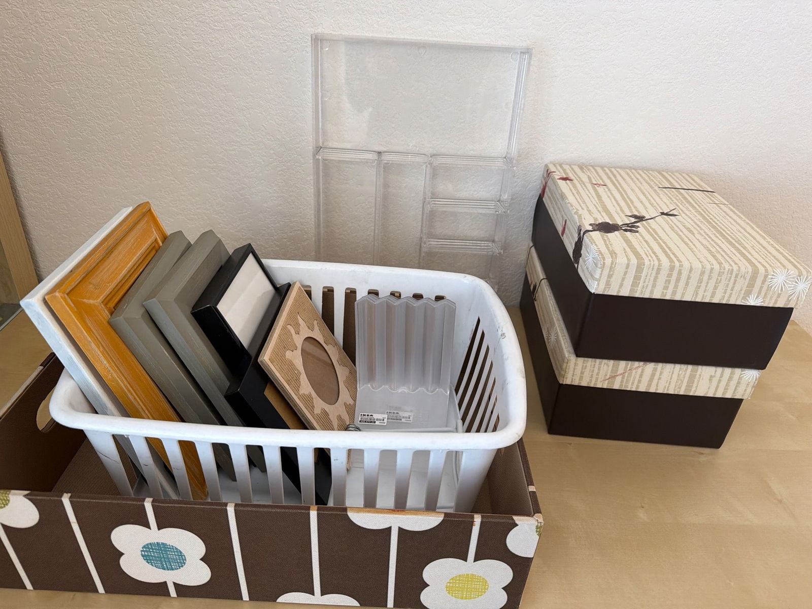 Photo Frames, Acrylic Organizer, and Decorative Boxes: A variety of photo frames in multiple colors and finishes contained in a white plastic basket with a decorative cover. Also included is an acrylic storage organizer with compartments for small items a