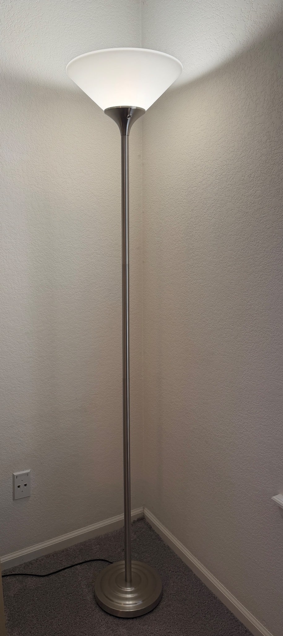Metal Torchiere Floor Lamp with Frosted Glass Shade: Metal torchiere floor lamp featuring a sleek, polished metal body and frosted white glass shade for ambient uplighting. The lamp is equipped with an electric cord and plug. A weighted base ensures sta