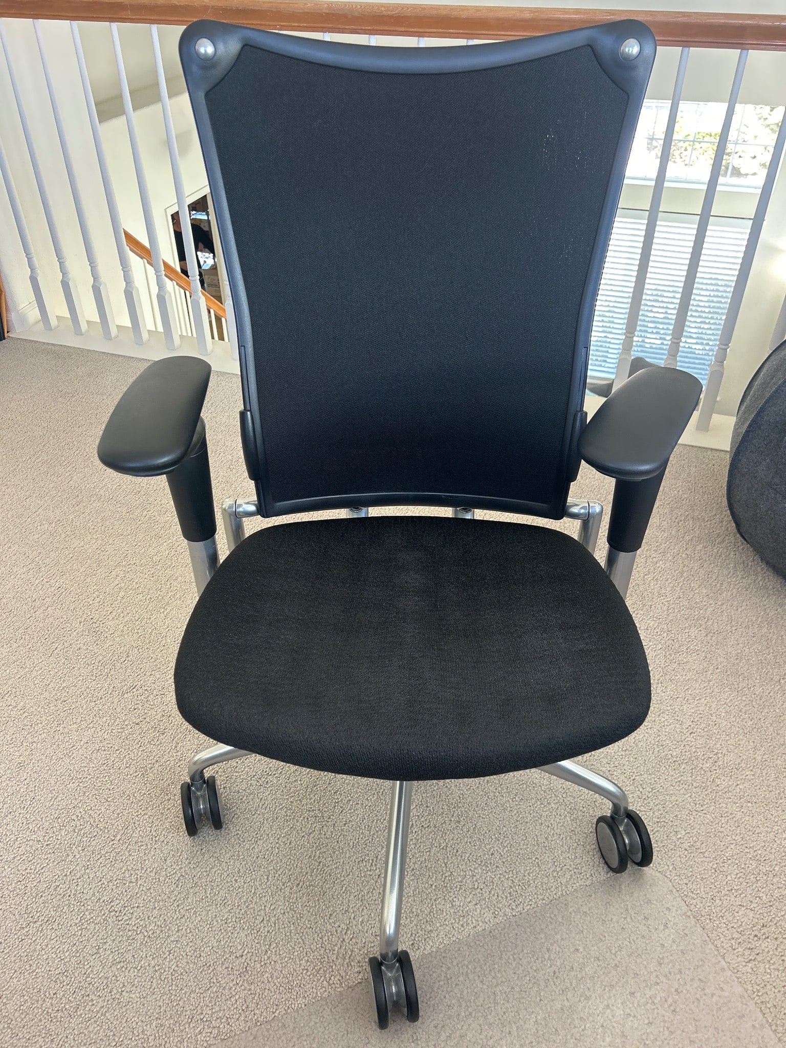 Allsteel Black Mesh Office Chair with Adjustable Armrests: Allsteel office chair featuring a black mesh backrest and cushioned black fabric seat. Equipped with adjustable armrests and a sculpted silver metal frame for ergonomic support. The chair sits on a fi