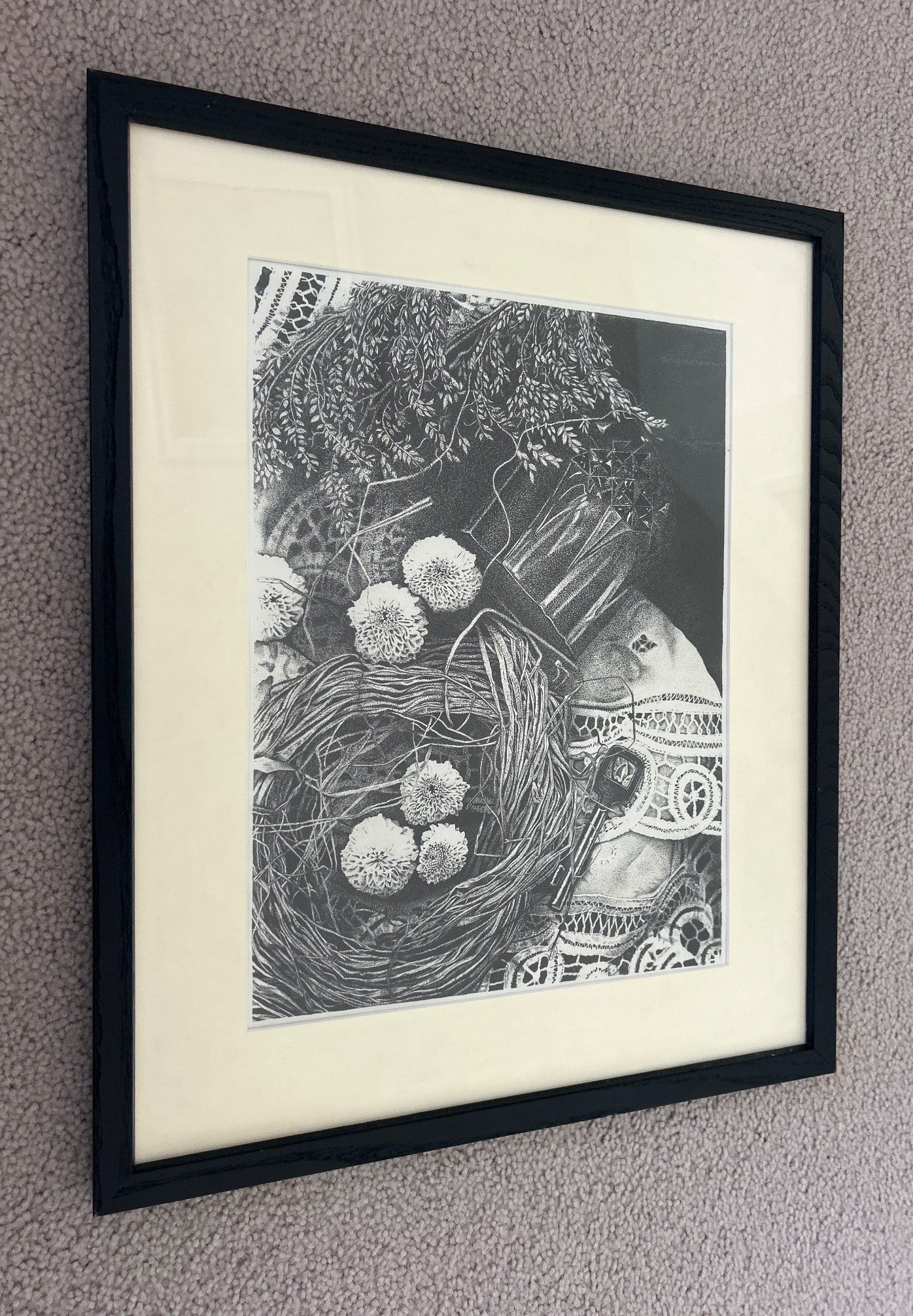 Framed Black-and-White Artwork Depicting a Birds Nest: Framed black-and-white artwork depicting a bird's nest surrounded by intricate textures, possibly printed or illustrated. Encased in a black wooden frame with a cream-colored matte. The back is equipp