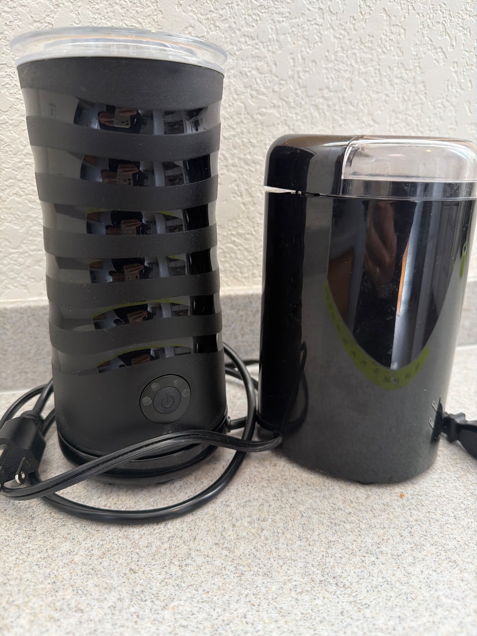Cuisinart Coffee Grinder and Electric Frother Set: A Cuisinart coffee grinder and an unidentified electric frother/milk frother. The coffee grinder is black with a clear lid and powered by a corded connection. The frother features a striped black desi