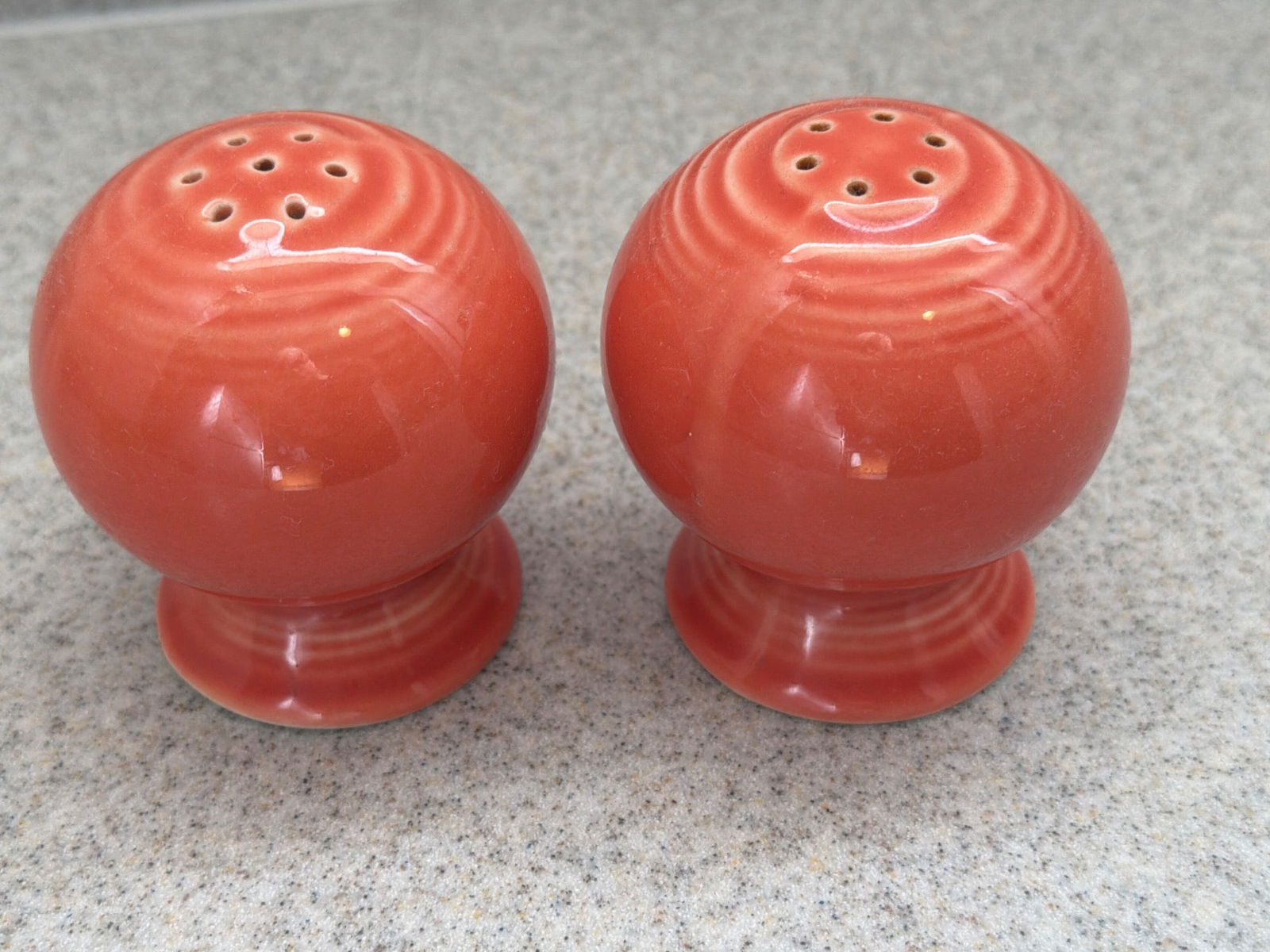 Fiesta Vintage Ceramic Orange Salt and Pepper Shakers: Vintage fiesta ceramic salt and pepper shakers in a vibrant orange color. Each shaker features a classic round shape with a pedestal base and multiple perforations on top for seasoning. They are in go