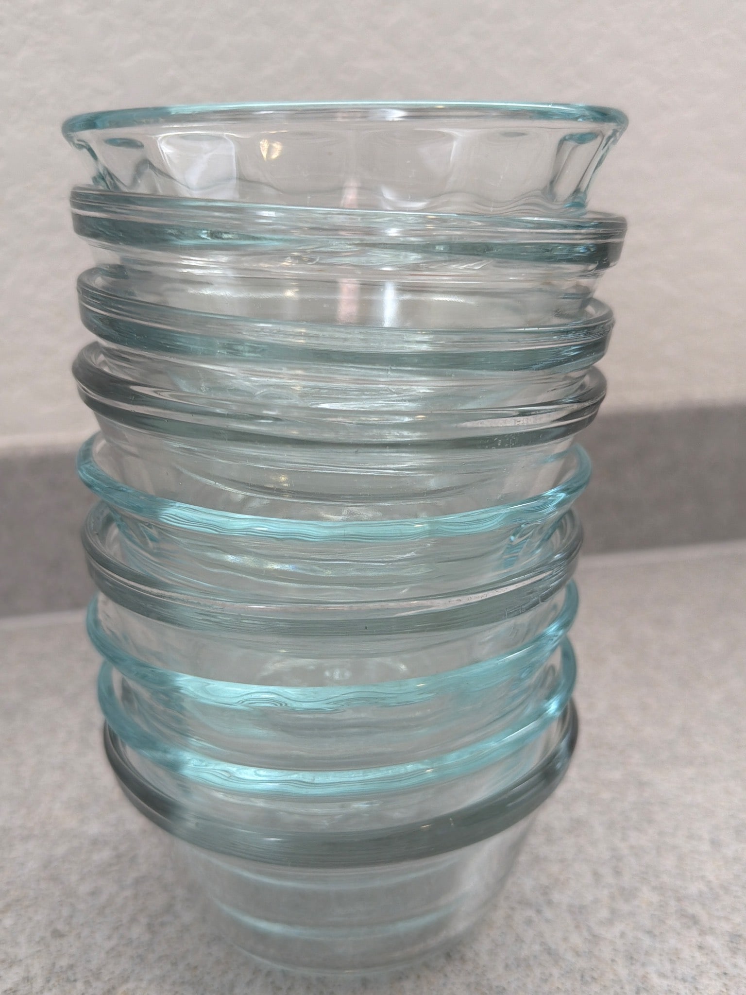 7 Clear Stacked Glass Bowls with Ribbed Accents: 7 clear glass bowls featuring ribbed accents along the exterior. These bowls display a stackable design, offering convenient storage. The glass is transparent with a light aqua tint. Suitable for serv