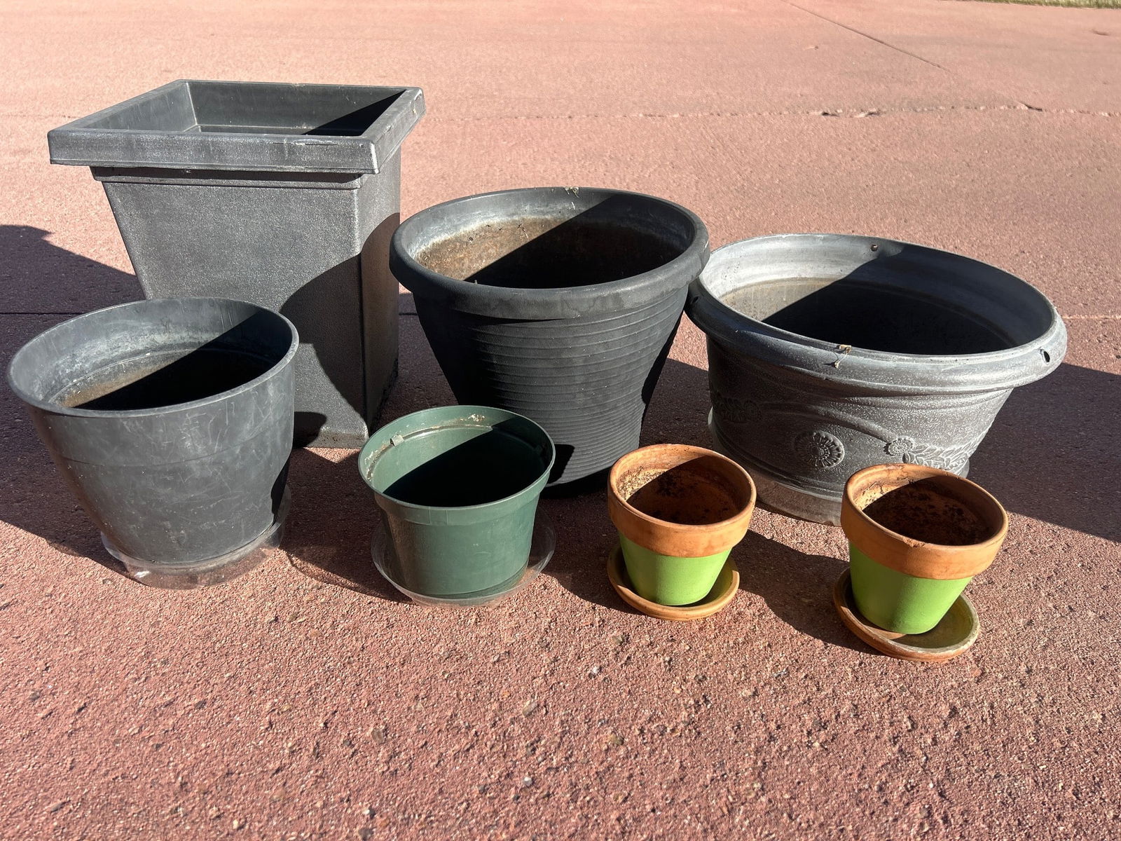 Seven Plastic and Ceramic Planter Pots: Seven planter pots, including five made of durable plastic in various sizes, shapes, and designs, and two ceramic pots with a glazed green finish and separate saucers. The plastic pots include both ro