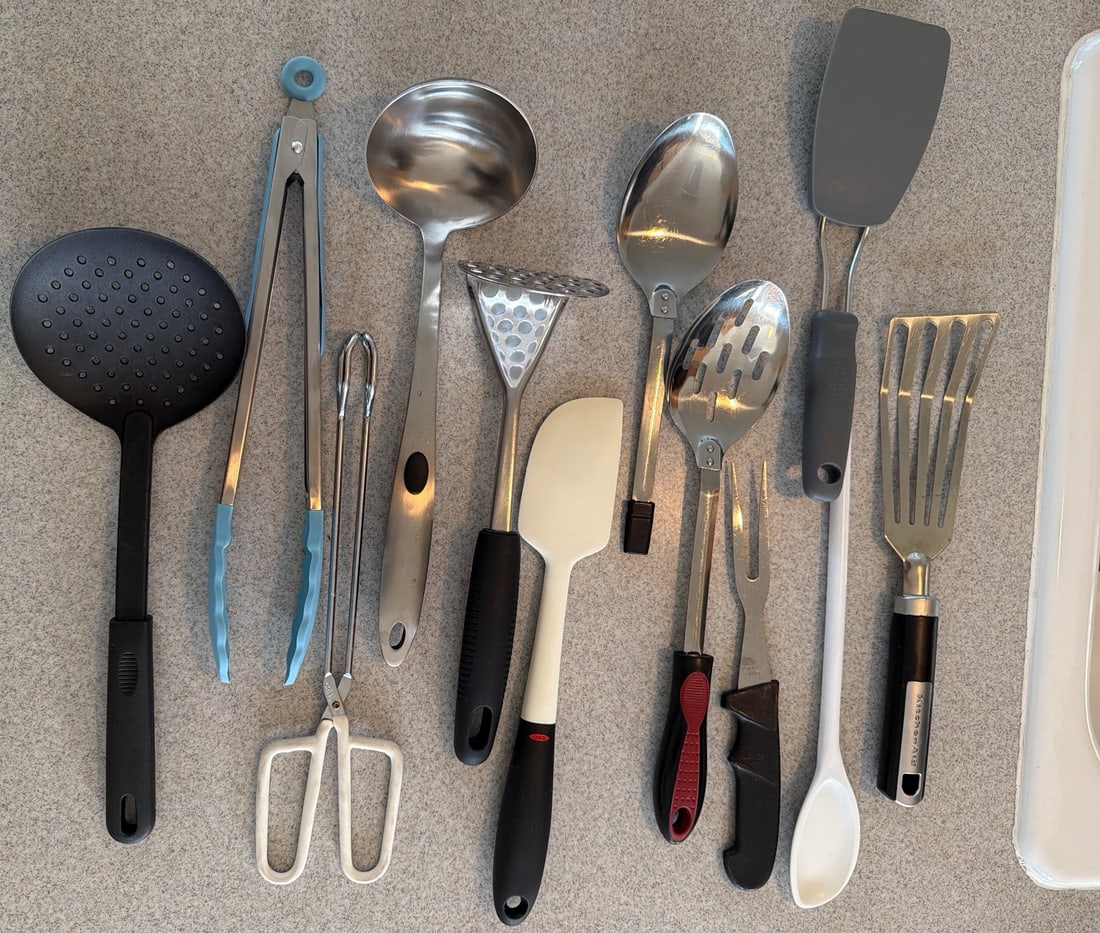 Kitchen Utensils Including Spatulas, Tongs, Ladles, and More: Kitchen utensils comprising various tools such as spatulas, ladles, tongs, serving spoons, and a potato masher. Items are constructed of stainless steel, plastic, and silicone. Includes both slotted a