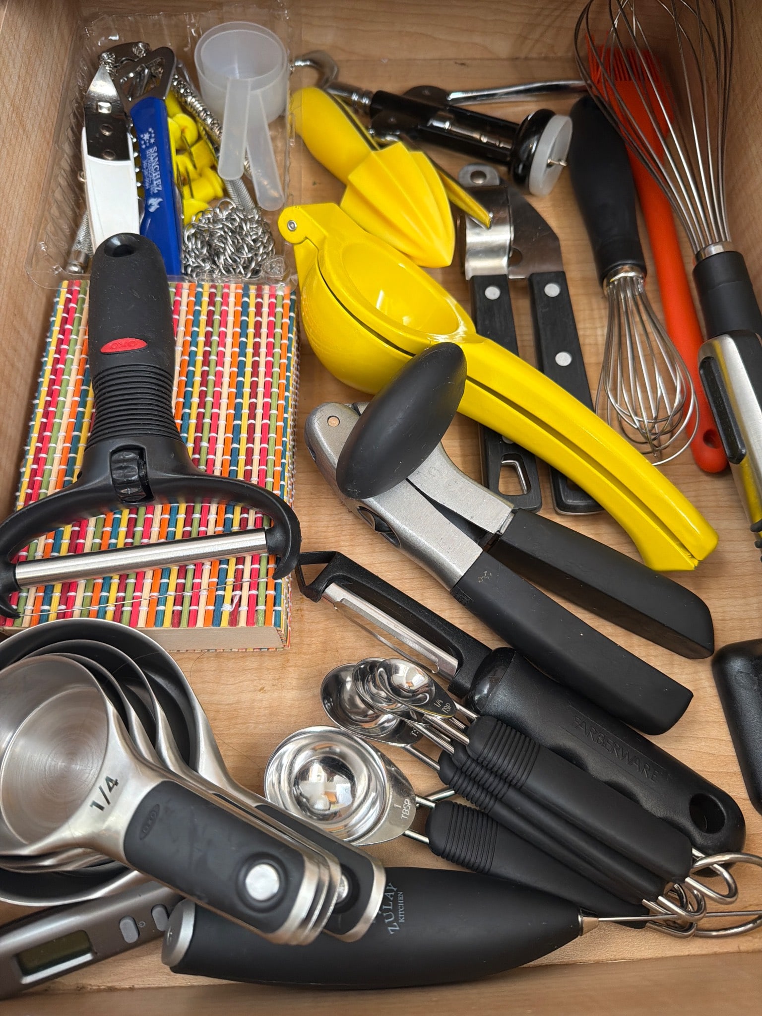 Kitchen Utensils, Including Juicers and Peelers: Kitchen utensils, including hand juicers, peelers, measuring spoons, whisks, and various gadgets. The items are constructed from metal and plastic materials, showcasing a mix of black, yellow, and sta