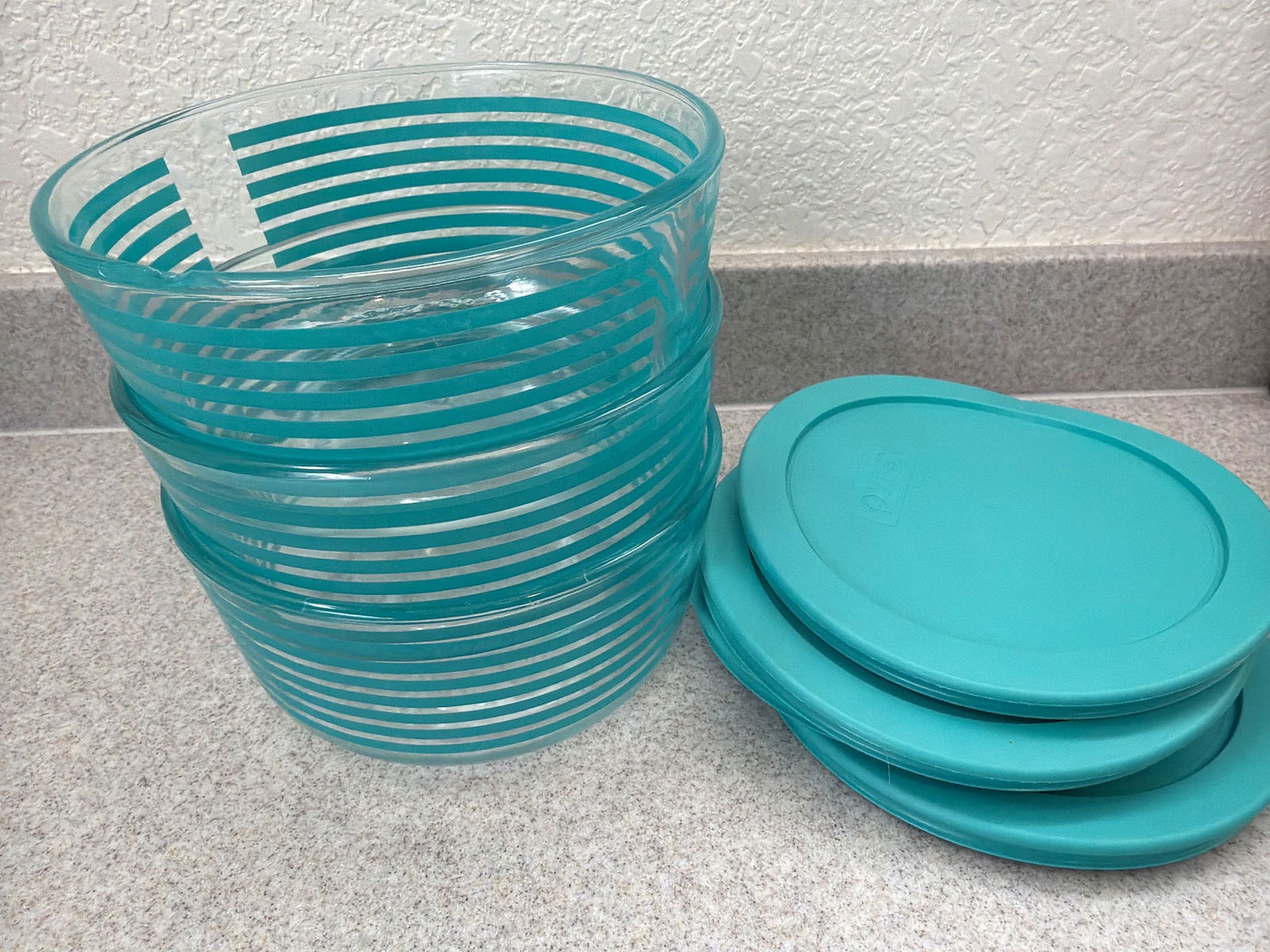 Pyrex Glass Bowls With Lids Featuring Teal Stripes- chip on one: Pyrex glass bowls featuring teal horizontal stripes, accompanied by matching teal plastic lids. Durable and versatile, suitable for storage and serving. Bowls are made of high-quality glass with embos
