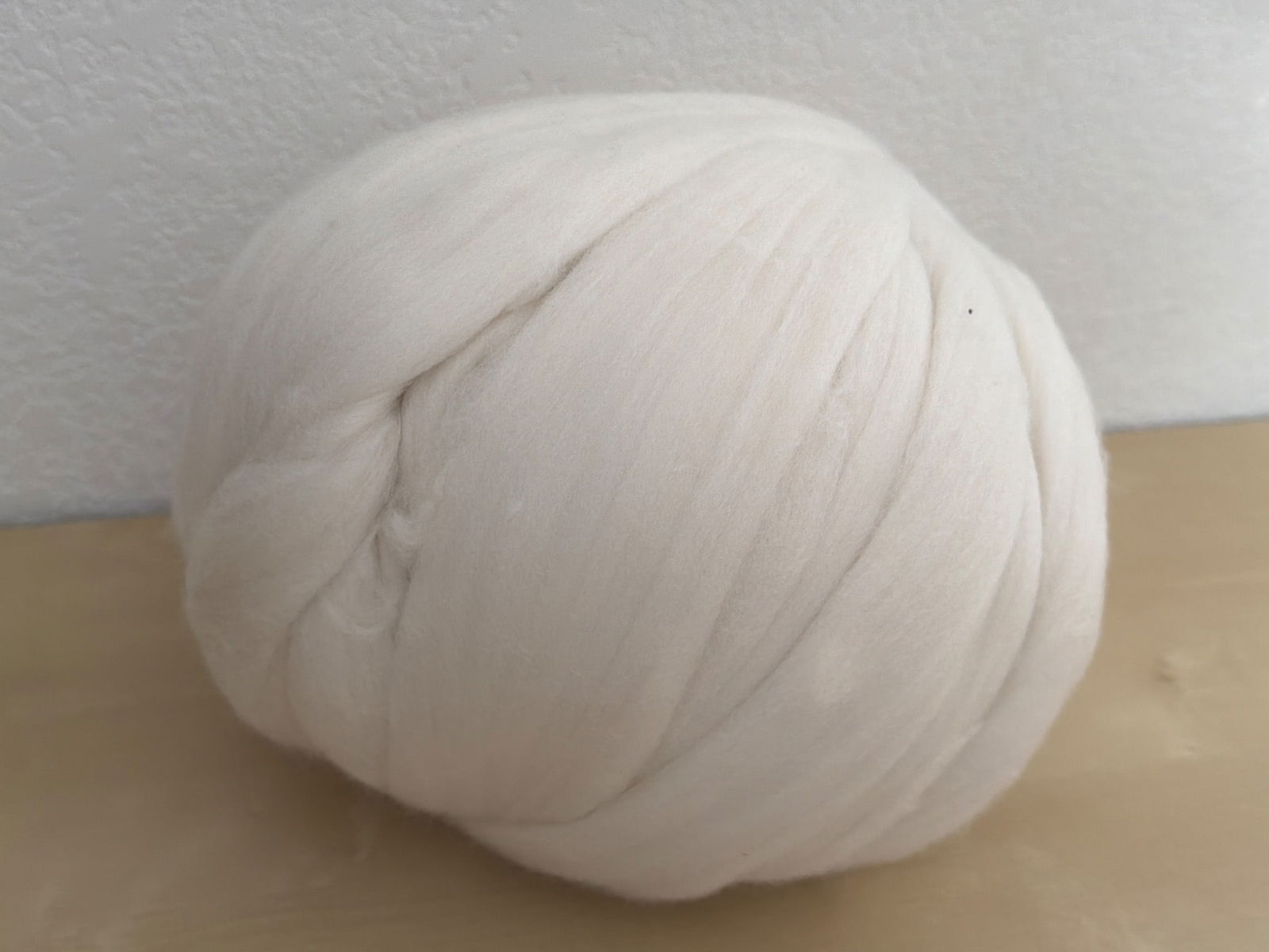 Cream-Colored Wool Roving Ball for Crafting or Spinning: Cream-colored wool roving ball, ideal for crafting, spinning, or felting projects. Soft and untwisted, it is suitable for various fiber art needs. The material appears to be natural wool, and it is in