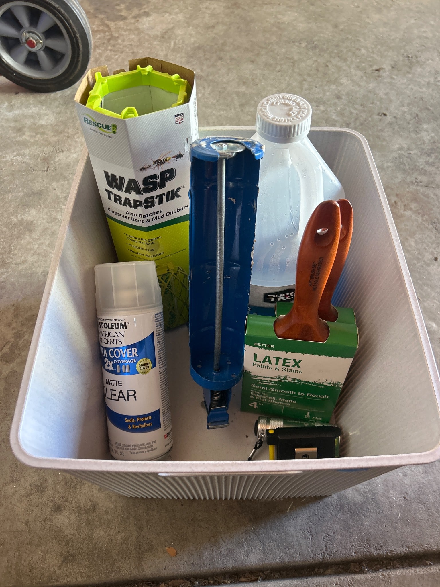 Household Tools, Paint Accessories, and Supplies in Storage Bin: A variety of household supplies, featuring a Wasp TrapStik, a can of Rust-Oleum Matte Clear spray (12 oz), a blue caulking gun, a two-pack of latex paintbrushes, a gallon of Super Tech Winter Formula